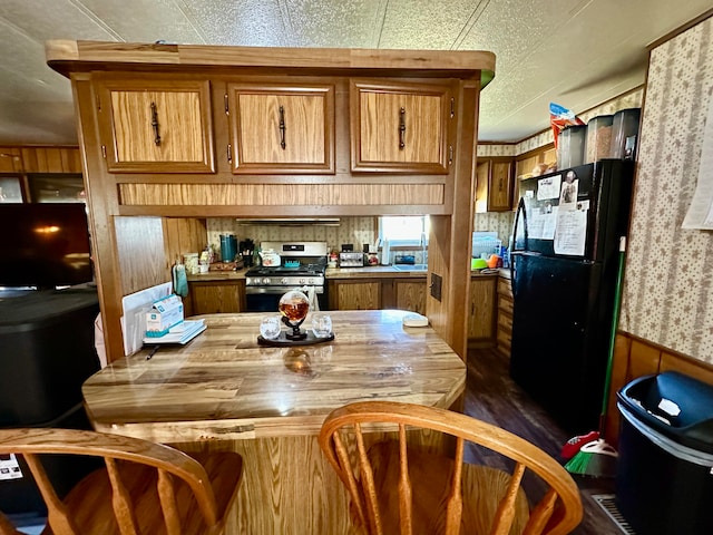 kitchen featuring wood counters, black fridge, stainless steel gas range oven, and wood walls