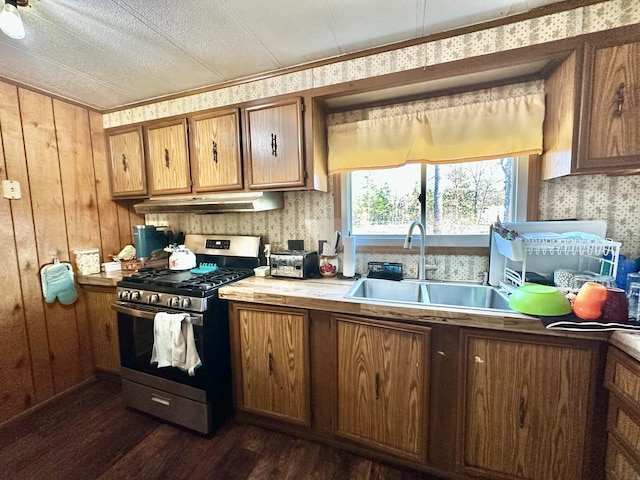 kitchen featuring a textured ceiling, dark wood-type flooring, sink, stainless steel gas stove, and wood walls