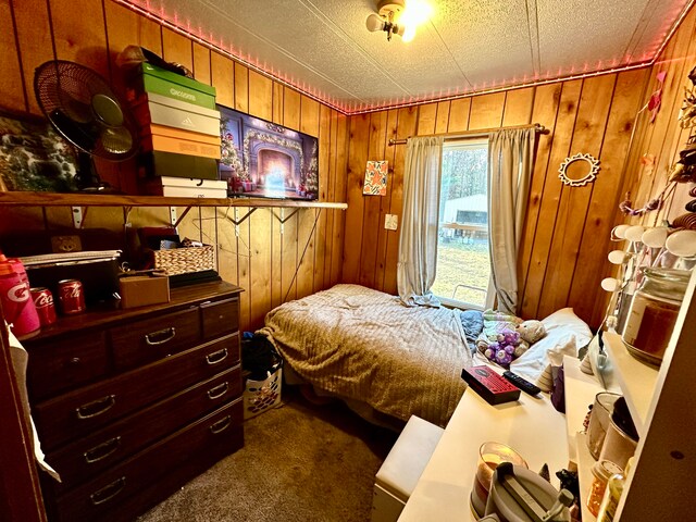 bedroom featuring a textured ceiling, dark carpet, and wooden walls