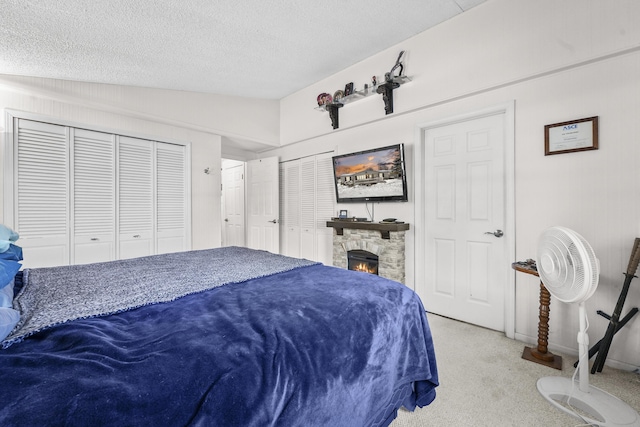 carpeted bedroom with a stone fireplace, lofted ceiling, and a textured ceiling