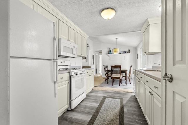 kitchen with white appliances, vaulted ceiling, sink, dark hardwood / wood-style floors, and white cabinetry