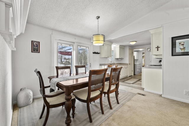 dining room with a textured ceiling, light colored carpet, lofted ceiling, and wood walls