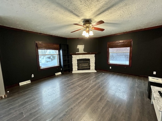 unfurnished living room featuring dark wood-type flooring, ceiling fan, ornamental molding, a textured ceiling, and a fireplace