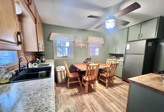 kitchen featuring stainless steel fridge, light wood-type flooring, ceiling fan, sink, and green cabinetry