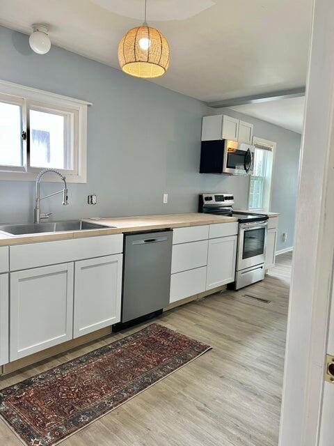 kitchen with light wood-type flooring, stainless steel appliances, sink, decorative light fixtures, and white cabinetry