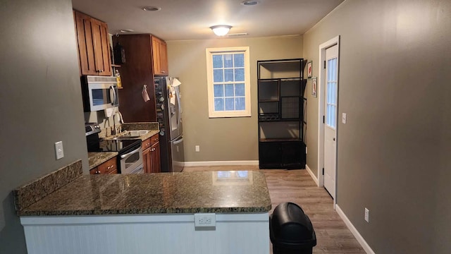 kitchen with sink, stainless steel appliances, kitchen peninsula, dark stone countertops, and light wood-type flooring