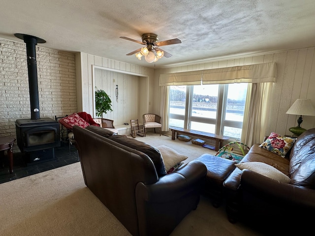 living room featuring carpet flooring, ceiling fan, a wood stove, and a textured ceiling