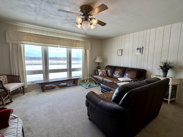 carpeted living room featuring ceiling fan, wood walls, a water view, and a textured ceiling