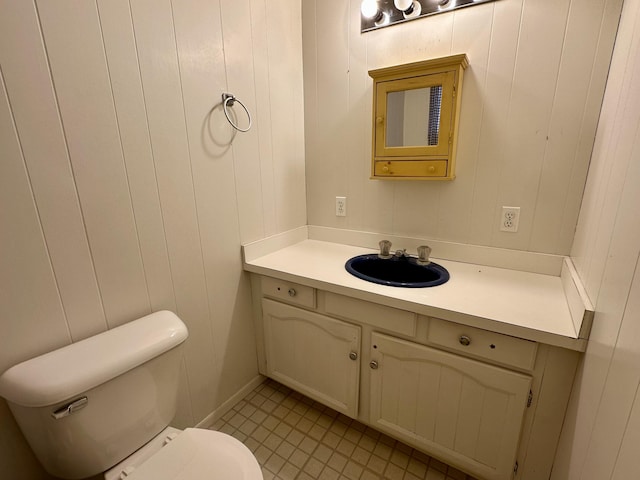 bathroom with tile patterned flooring, vanity, wood walls, and toilet