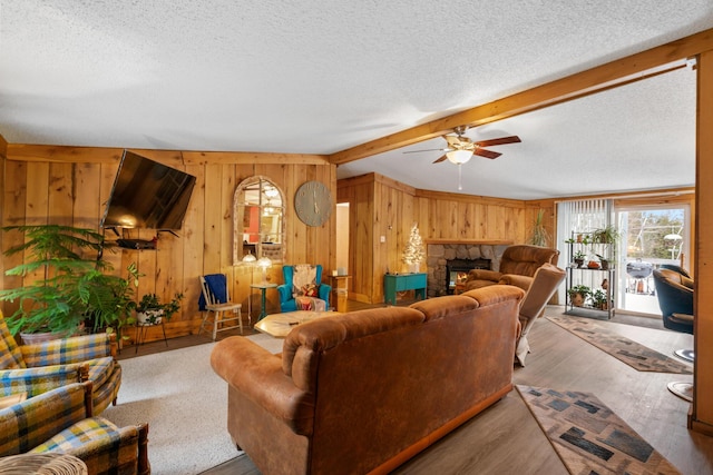 living room with ceiling fan, beam ceiling, a fireplace, and wooden walls