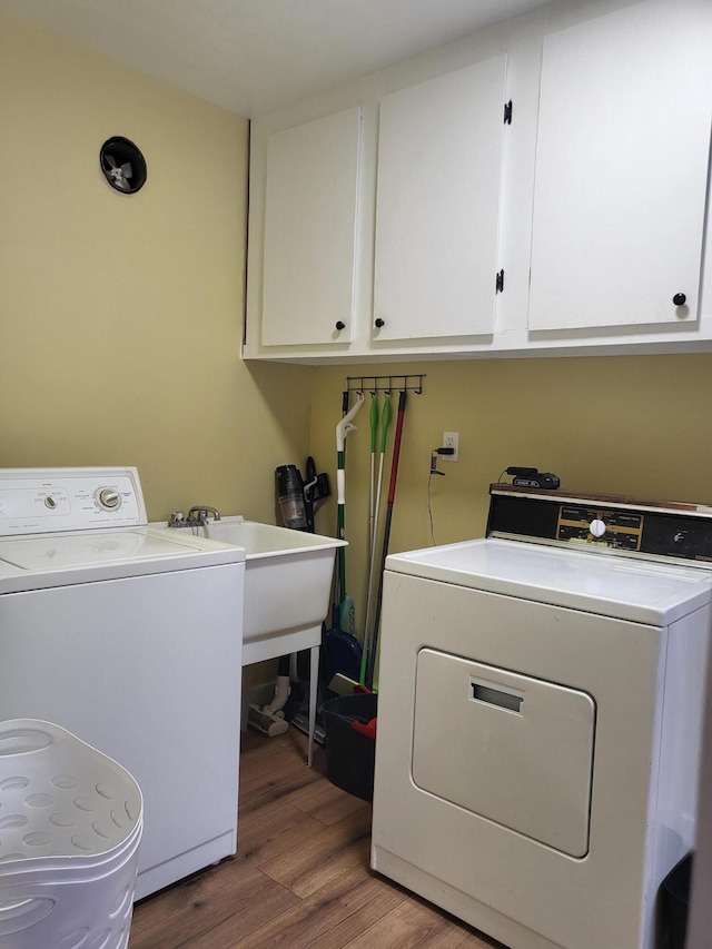 clothes washing area with washer and clothes dryer, cabinets, sink, and hardwood / wood-style flooring