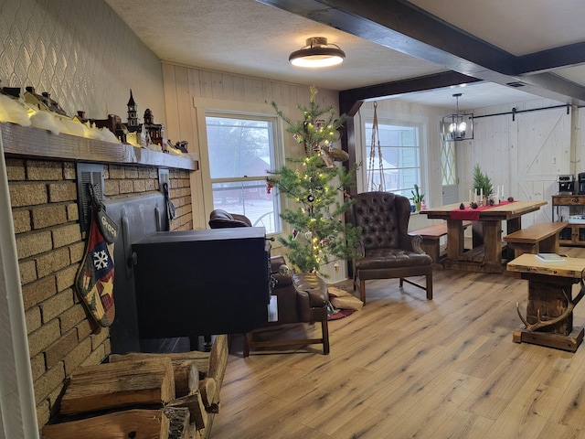 living room with beamed ceiling, a barn door, light hardwood / wood-style floors, and a notable chandelier