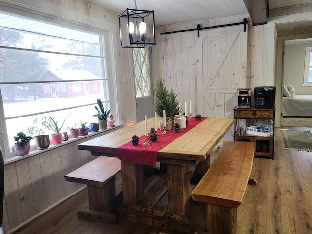 dining space with a barn door, wooden walls, and hardwood / wood-style flooring