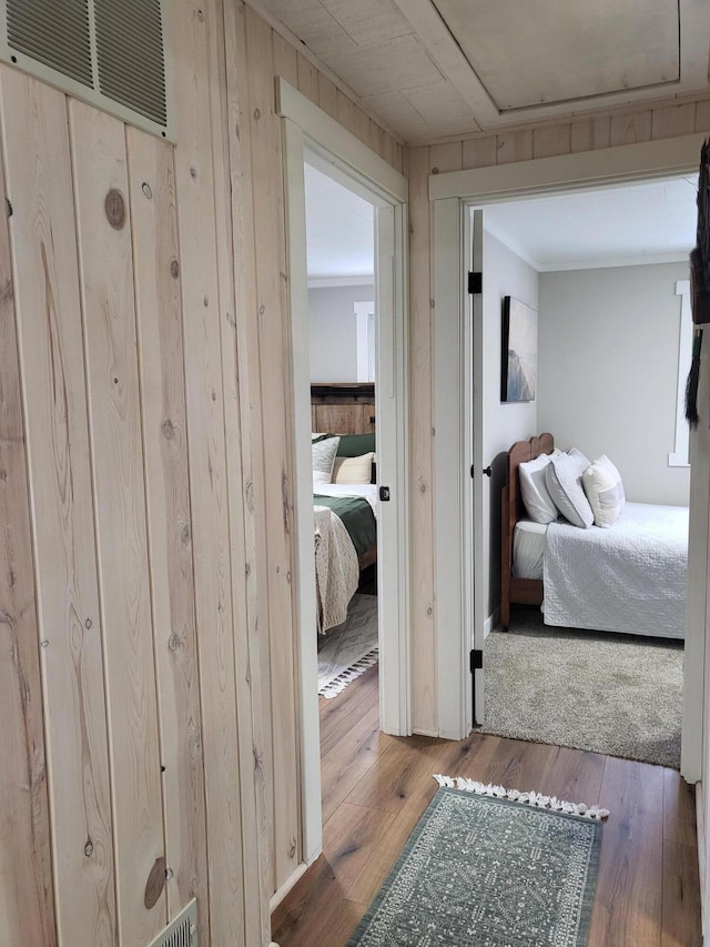 hallway featuring hardwood / wood-style floors, ornamental molding, and wooden walls