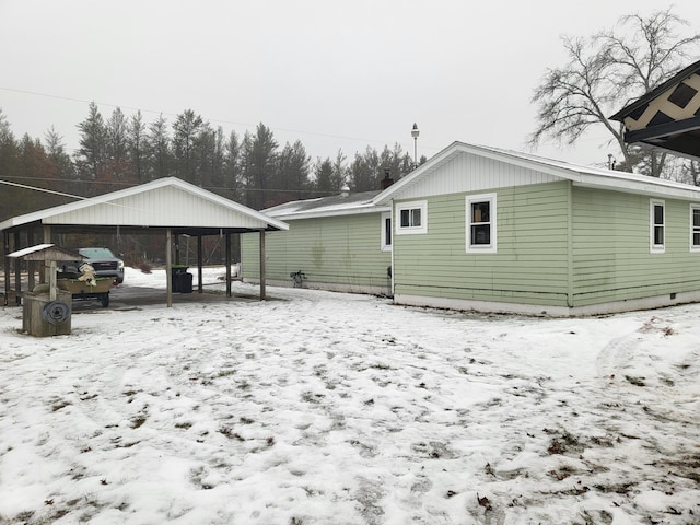 snow covered rear of property featuring a carport