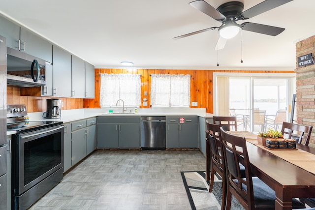 kitchen featuring light parquet flooring, stainless steel appliances, ceiling fan, wooden walls, and sink