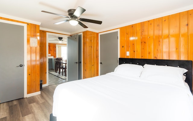 bedroom featuring ornamental molding, ceiling fan, wood walls, and hardwood / wood-style flooring