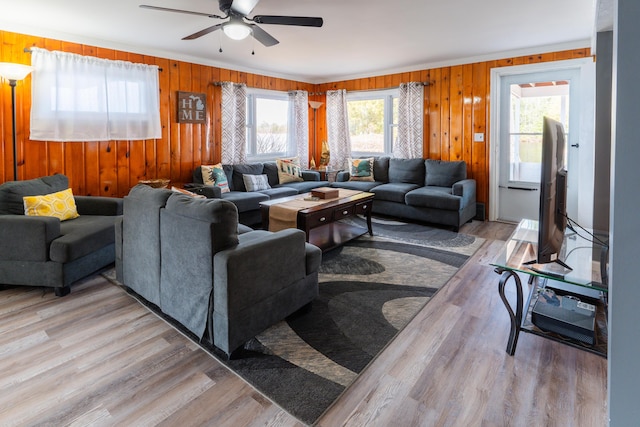 living room with wood walls, ceiling fan, and light hardwood / wood-style flooring