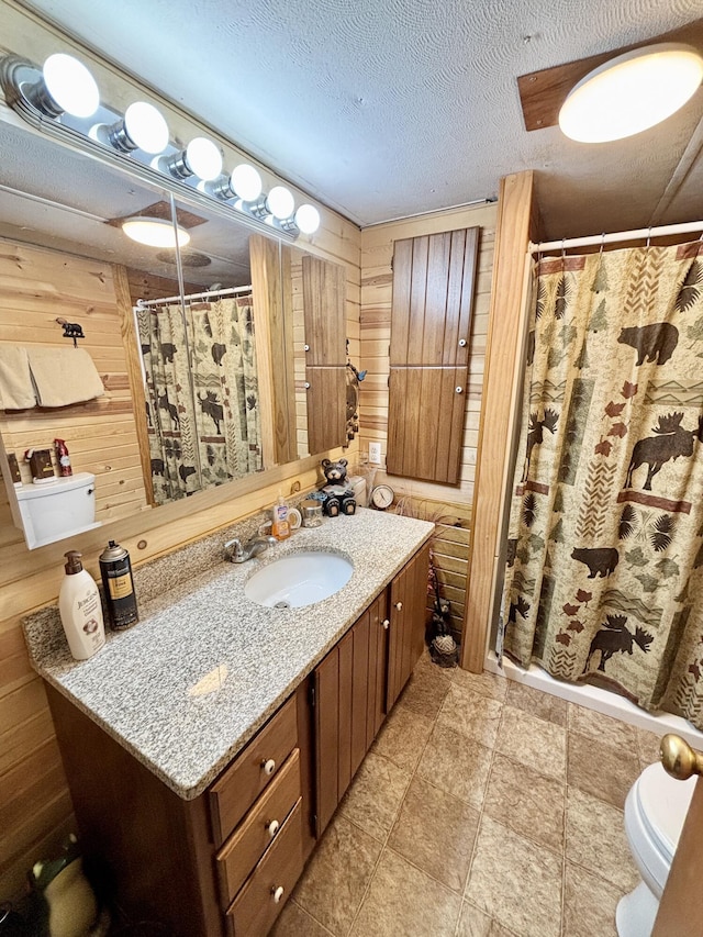 bathroom featuring vanity, a textured ceiling, curtained shower, toilet, and wood walls