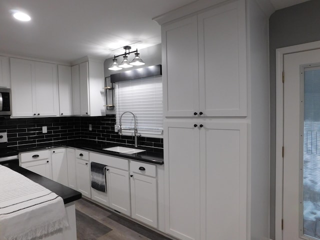 kitchen with stove, backsplash, white cabinetry, and sink