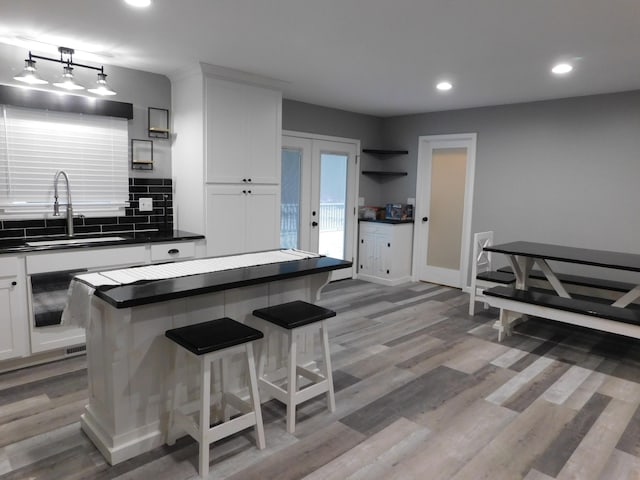 kitchen featuring french doors, sink, light wood-type flooring, a kitchen island, and white cabinetry