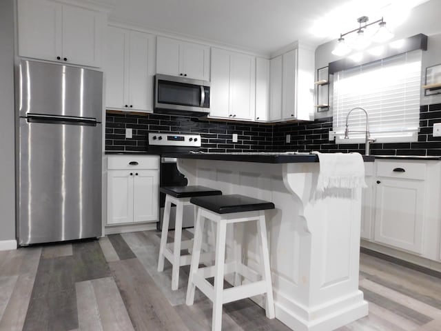 kitchen featuring wood-type flooring, tasteful backsplash, a kitchen island, white cabinetry, and stainless steel appliances