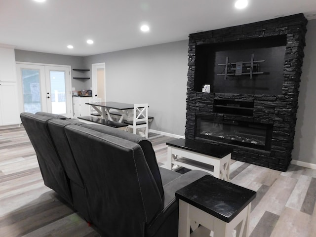 living room with french doors, light wood-type flooring, and a stone fireplace