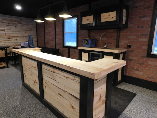 bar featuring butcher block counters, light brown cabinetry, brick wall, and decorative light fixtures