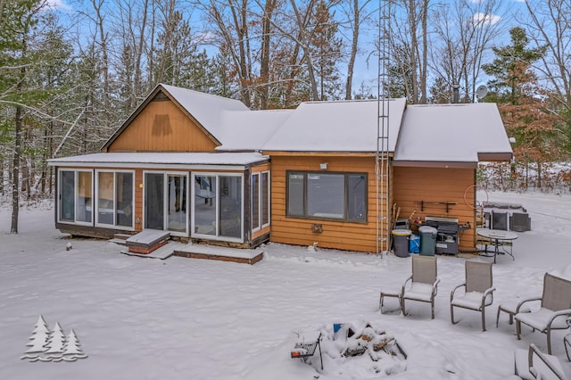 snow covered rear of property with a sunroom