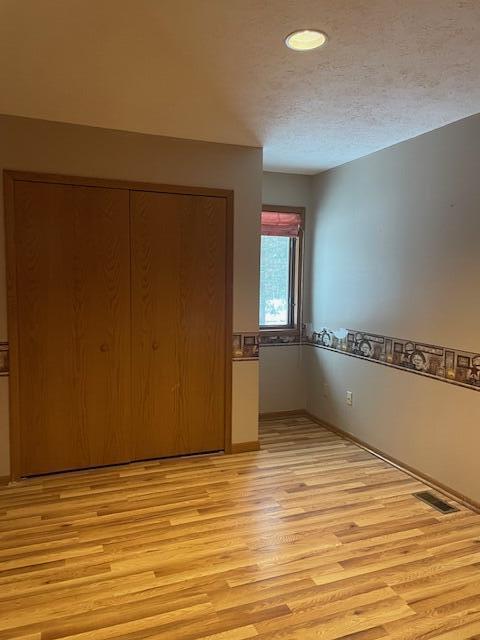 unfurnished bedroom featuring a textured ceiling, light hardwood / wood-style flooring, and a closet