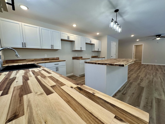 kitchen featuring sink, decorative light fixtures, white cabinetry, a center island, and butcher block countertops