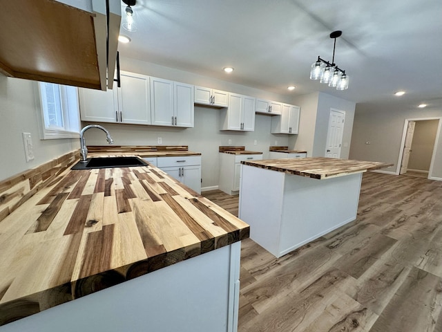 kitchen featuring wood counters, pendant lighting, a kitchen island, sink, and white cabinetry