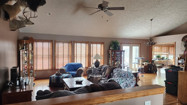 living room with lofted ceiling, light wood finished floors, a textured ceiling, and ceiling fan with notable chandelier