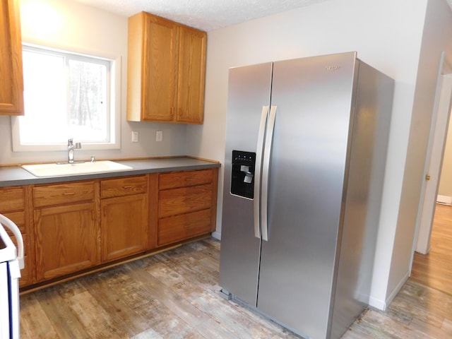 kitchen featuring sink, stainless steel refrigerator with ice dispenser, a textured ceiling, light hardwood / wood-style floors, and range