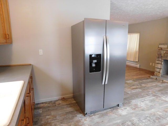 kitchen with stainless steel refrigerator with ice dispenser, a textured ceiling, light hardwood / wood-style flooring, and a stone fireplace