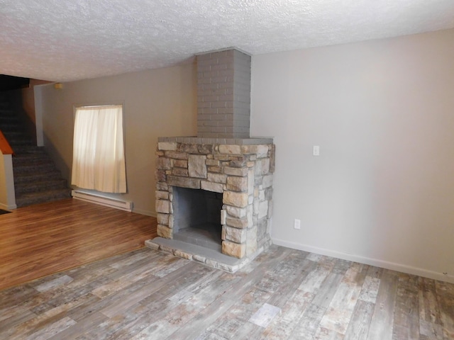 unfurnished living room with hardwood / wood-style floors, a stone fireplace, a textured ceiling, and a baseboard heating unit