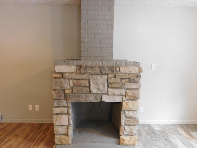 interior details with a textured ceiling, hardwood / wood-style flooring, and a stone fireplace