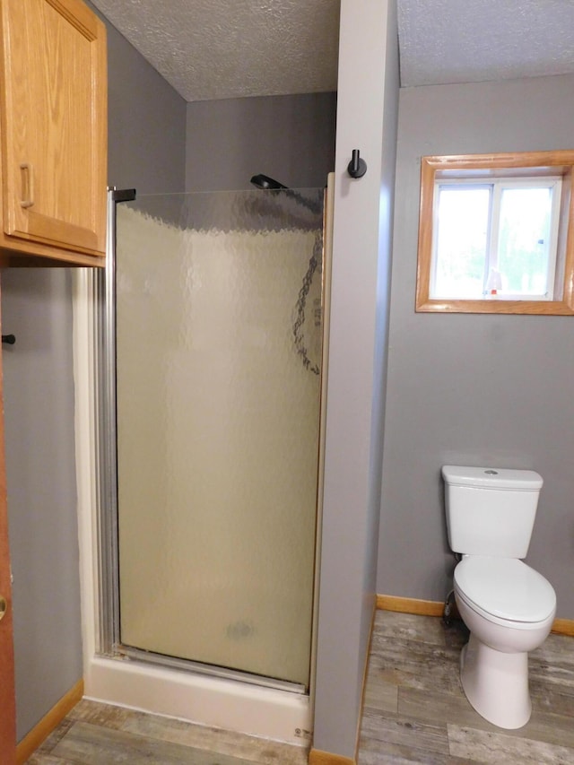 bathroom with hardwood / wood-style flooring, a shower with shower door, a textured ceiling, and toilet