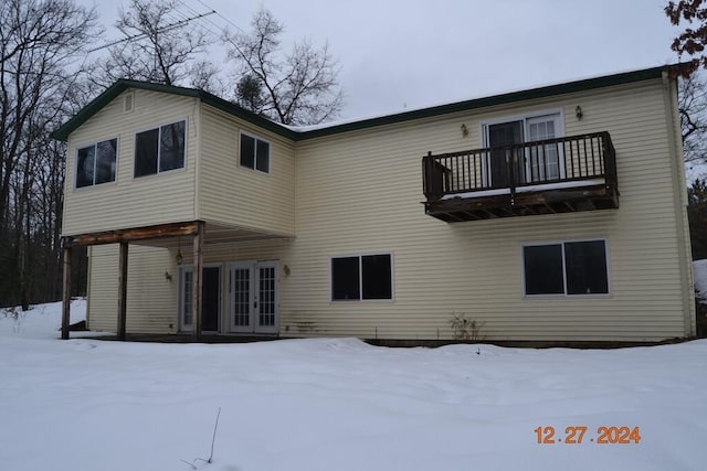 snow covered back of property with a balcony and french doors