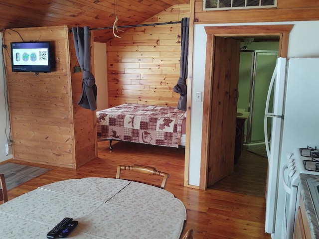 bedroom featuring wooden ceiling, white fridge, lofted ceiling, wooden walls, and hardwood / wood-style flooring