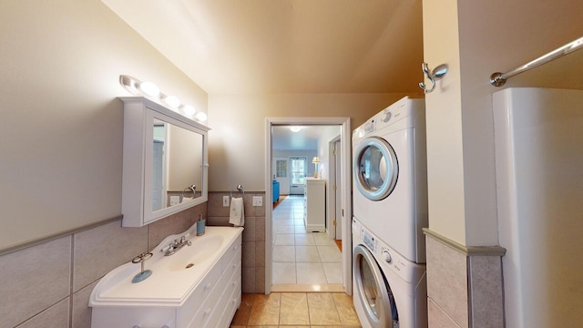 laundry room featuring sink, stacked washing maching and dryer, tile walls, and light tile patterned flooring