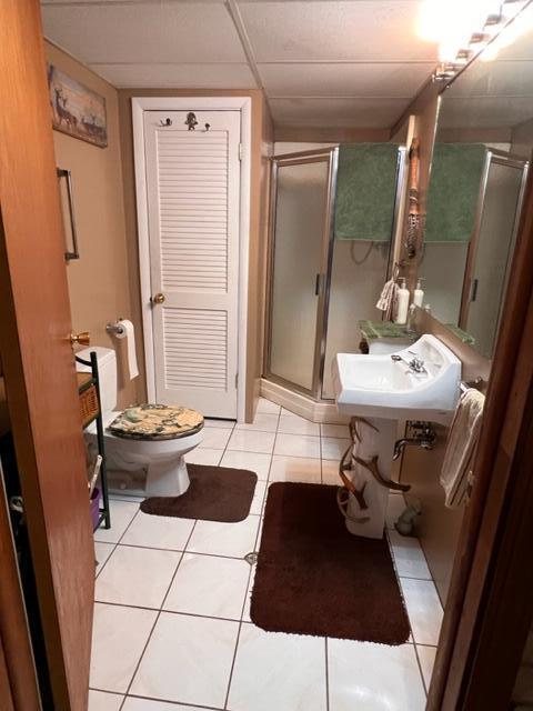 bathroom with a drop ceiling, sink, tile patterned floors, an enclosed shower, and toilet