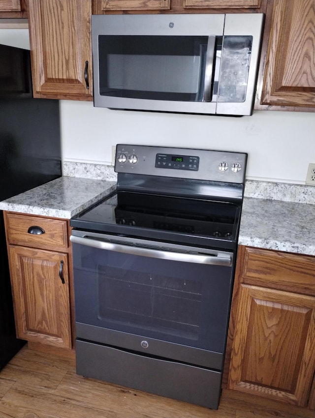 kitchen with appliances with stainless steel finishes, light hardwood / wood-style floors, and light stone counters