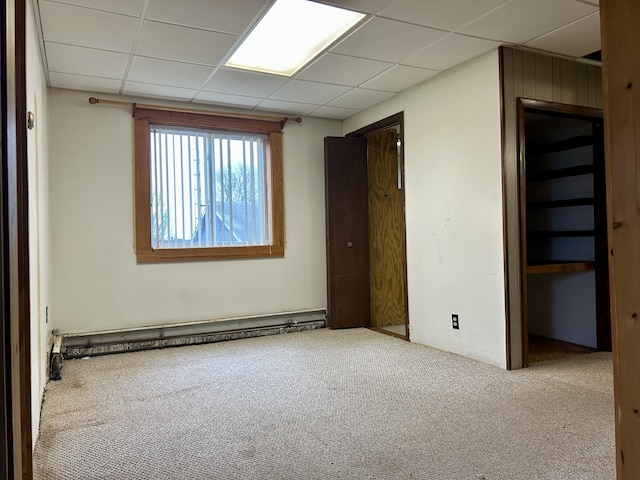 carpeted empty room with a drop ceiling and a baseboard heating unit