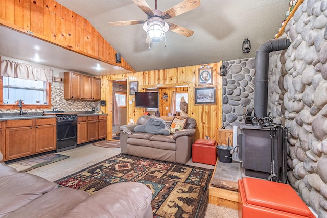 living room featuring lofted ceiling, ceiling fan, a wood stove, and sink