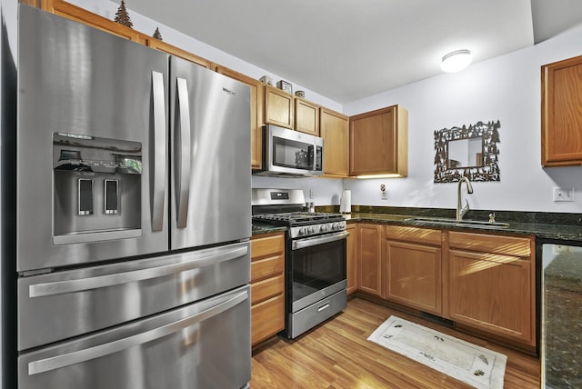 kitchen with dark stone counters, sink, stainless steel appliances, and light hardwood / wood-style floors