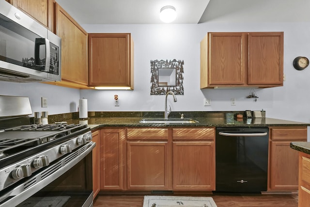 kitchen with appliances with stainless steel finishes, dark hardwood / wood-style floors, dark stone countertops, and sink