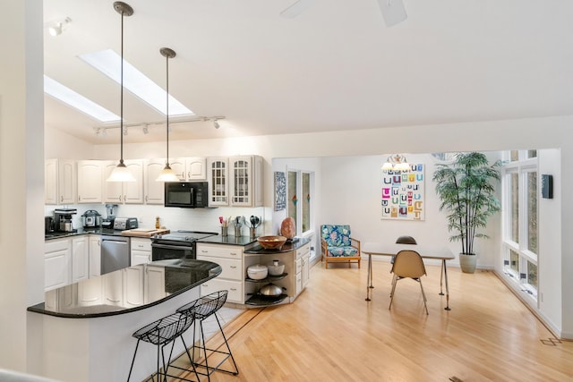 kitchen with a skylight, black appliances, light hardwood / wood-style flooring, white cabinets, and hanging light fixtures