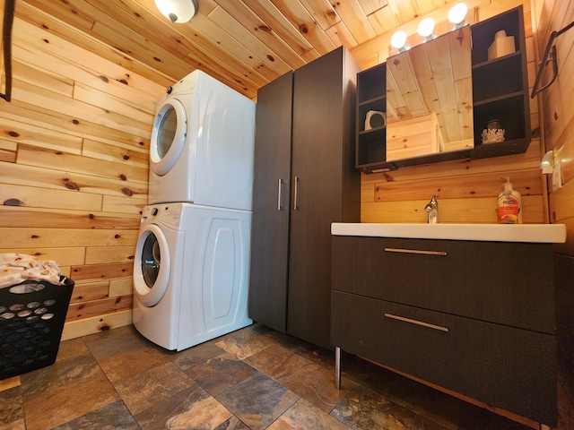 washroom featuring stacked washing maching and dryer, wood ceiling, sink, and wooden walls