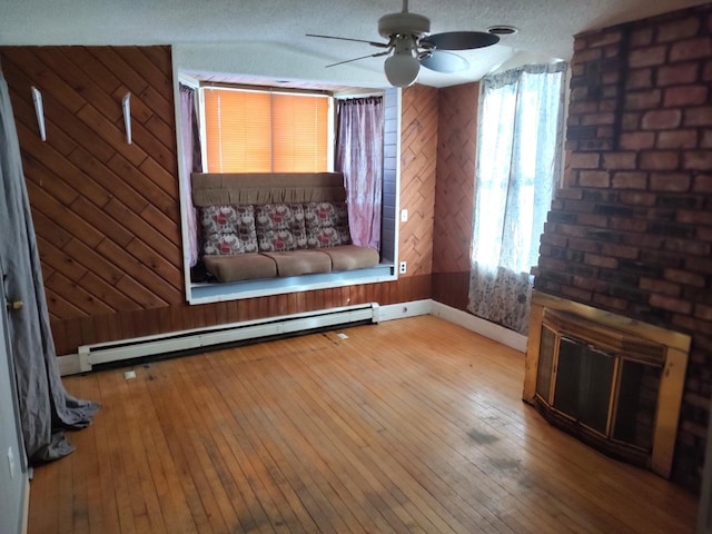 interior space with ceiling fan, baseboard heating, a textured ceiling, wooden walls, and a fireplace